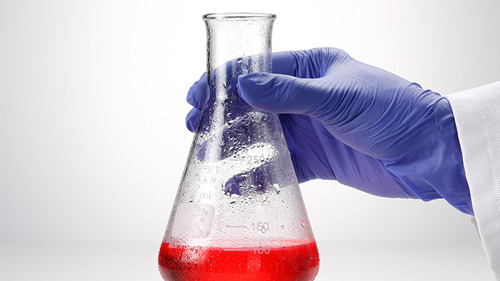 A hand in a purple glove holds a flask with chemicals and red liquid, symbolizing safety for the StarGuard® Sensitive Starlabs brand.